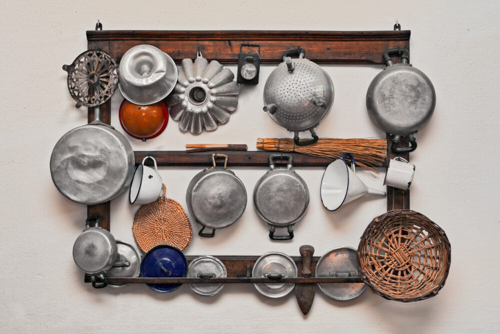 White-walled kitchen, vintage cookware rack, organized rows, soft daylight, editorial travel photo, no people.