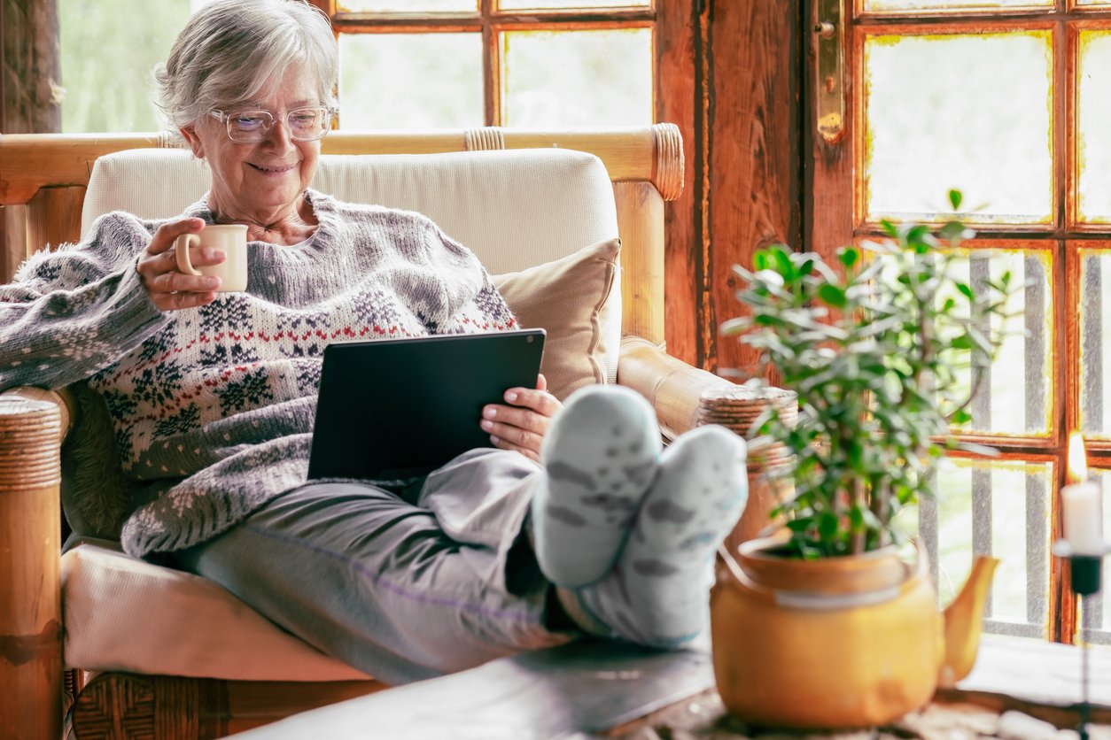 Living room, elderly woman with mug and tablet, wide cozy setting, bright morning light, documentary style, single person.