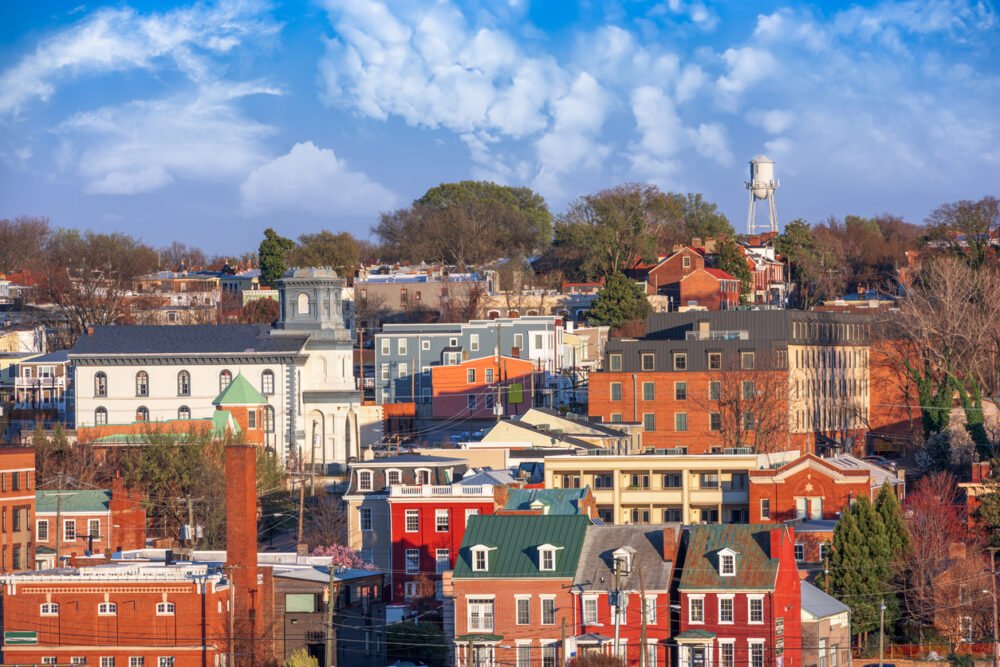 Small cityscape, historic colorful buildings, water tower background, blue sky midday, editorial travel photo, no people.