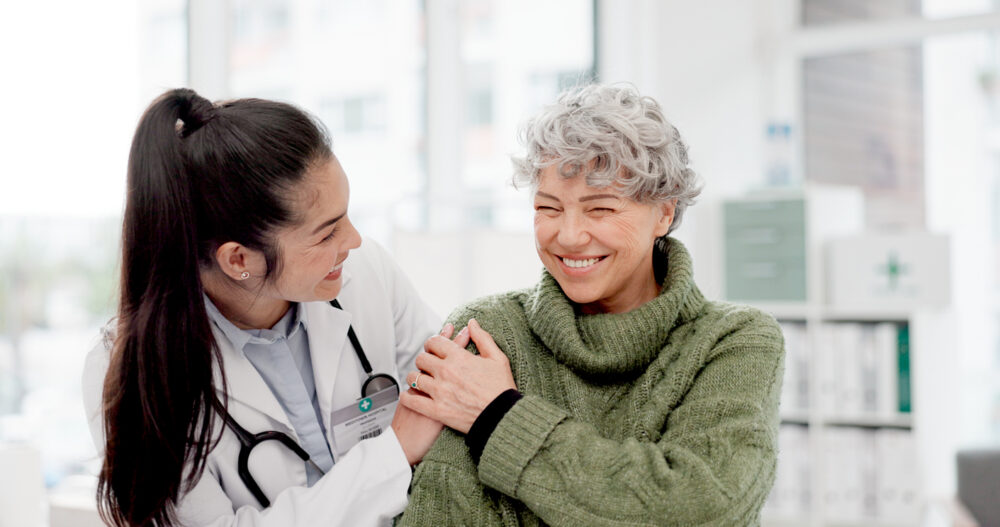 Bright medical office interior, doctor with stethoscope and elderly woman, close interaction, daylight, documentary style, people.