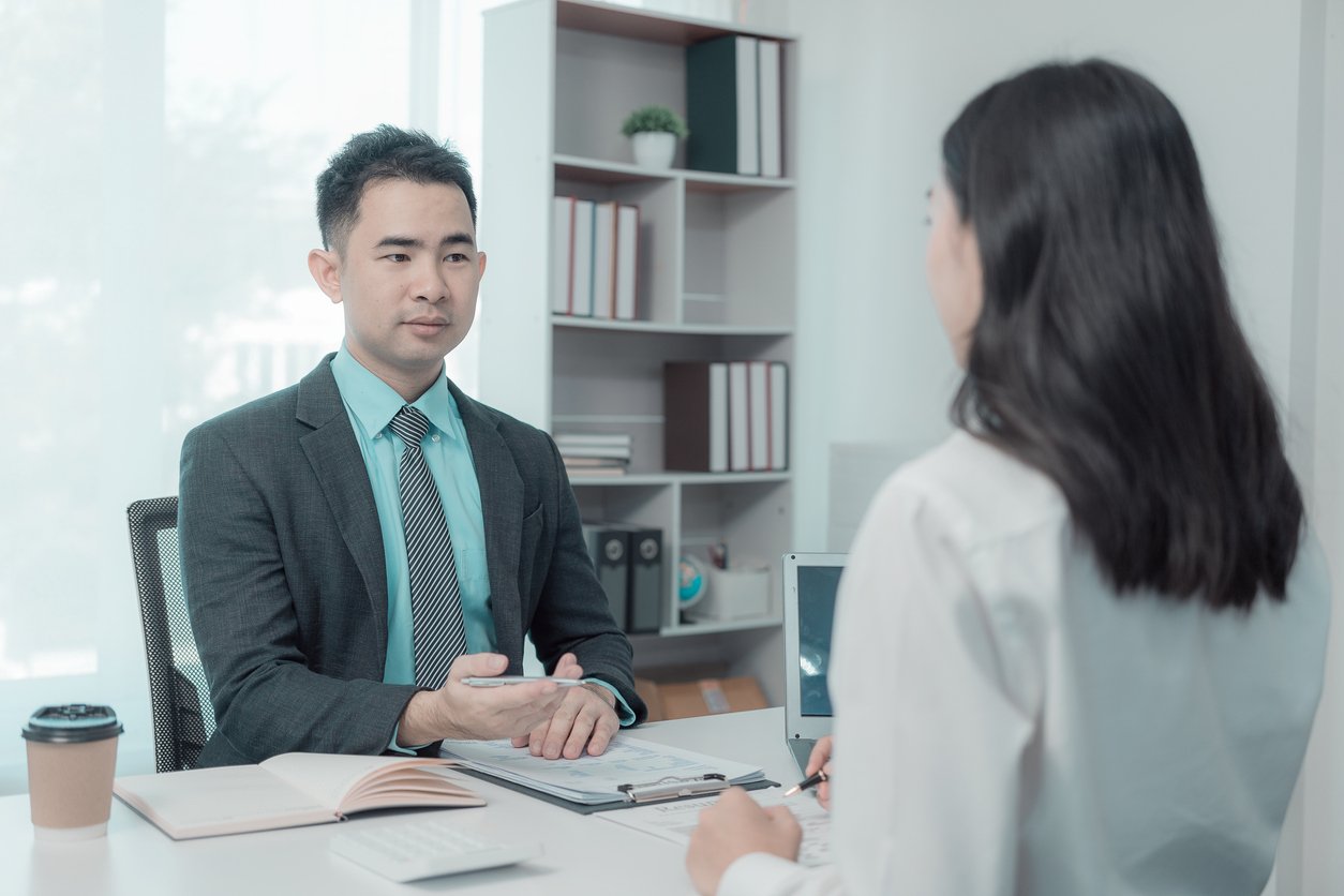 Bright office, desk with open notebook and pen, mid-shot composition, natural daylight, documentary style, two people.