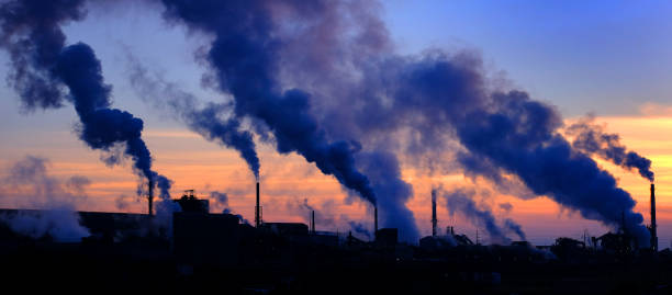 Factory rooftop, smokestacks billowing smoke, strong silhouettes against vibrant sunset, evening glow, editorial travel photo, no people.