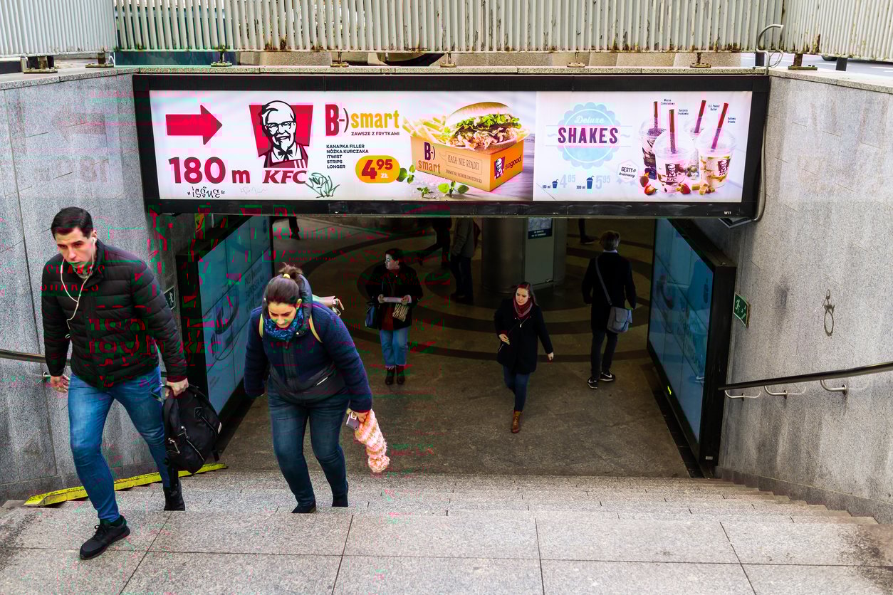 Subway underpass, KFC B Smart ad, stairs and arrow, daytime lighting, editorial travel photo, people present.
