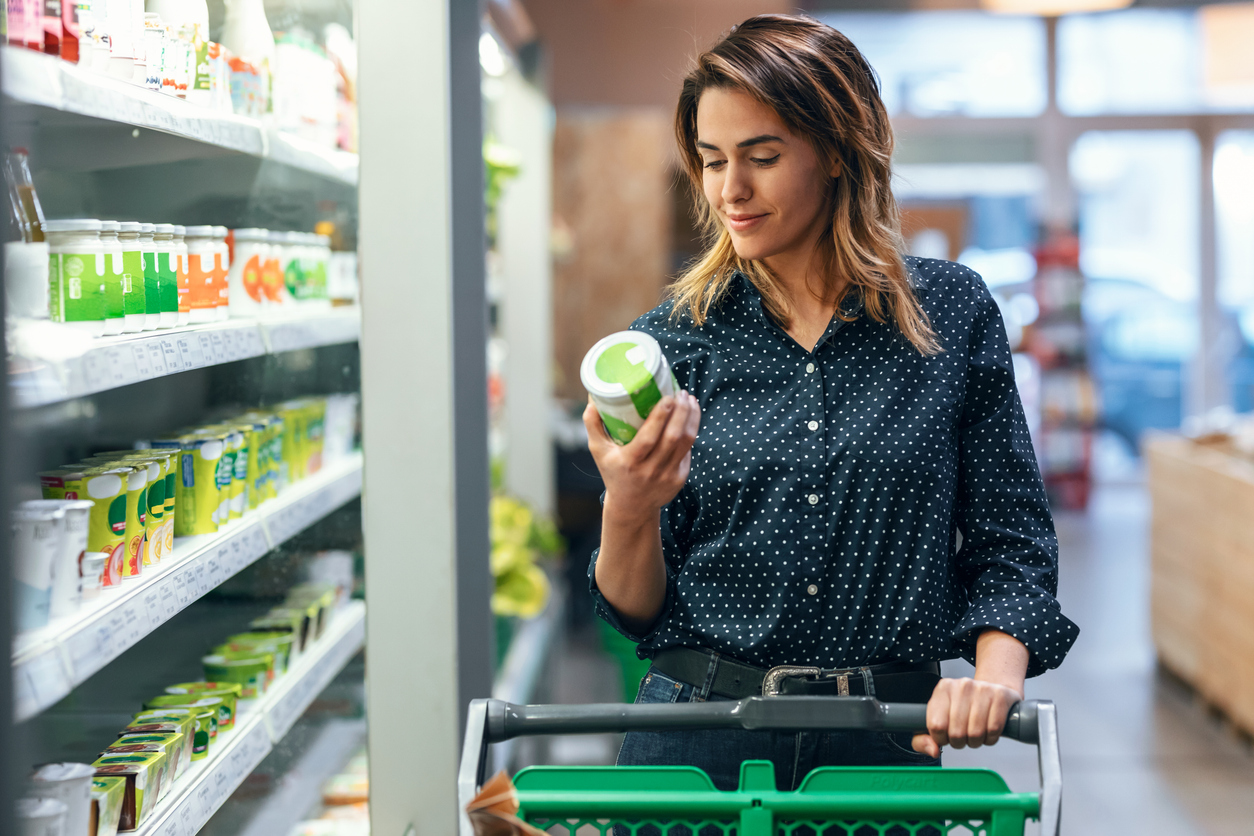 Grocery store aisle, woman checks product label, mid-shot, bright overhead lights, editorial travel photo, one person.