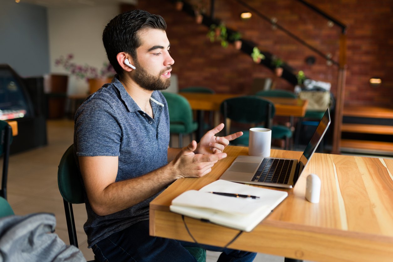 Cafe interior, man with earbuds at table, laptop open, morning light, editorial travel photo, single person present.