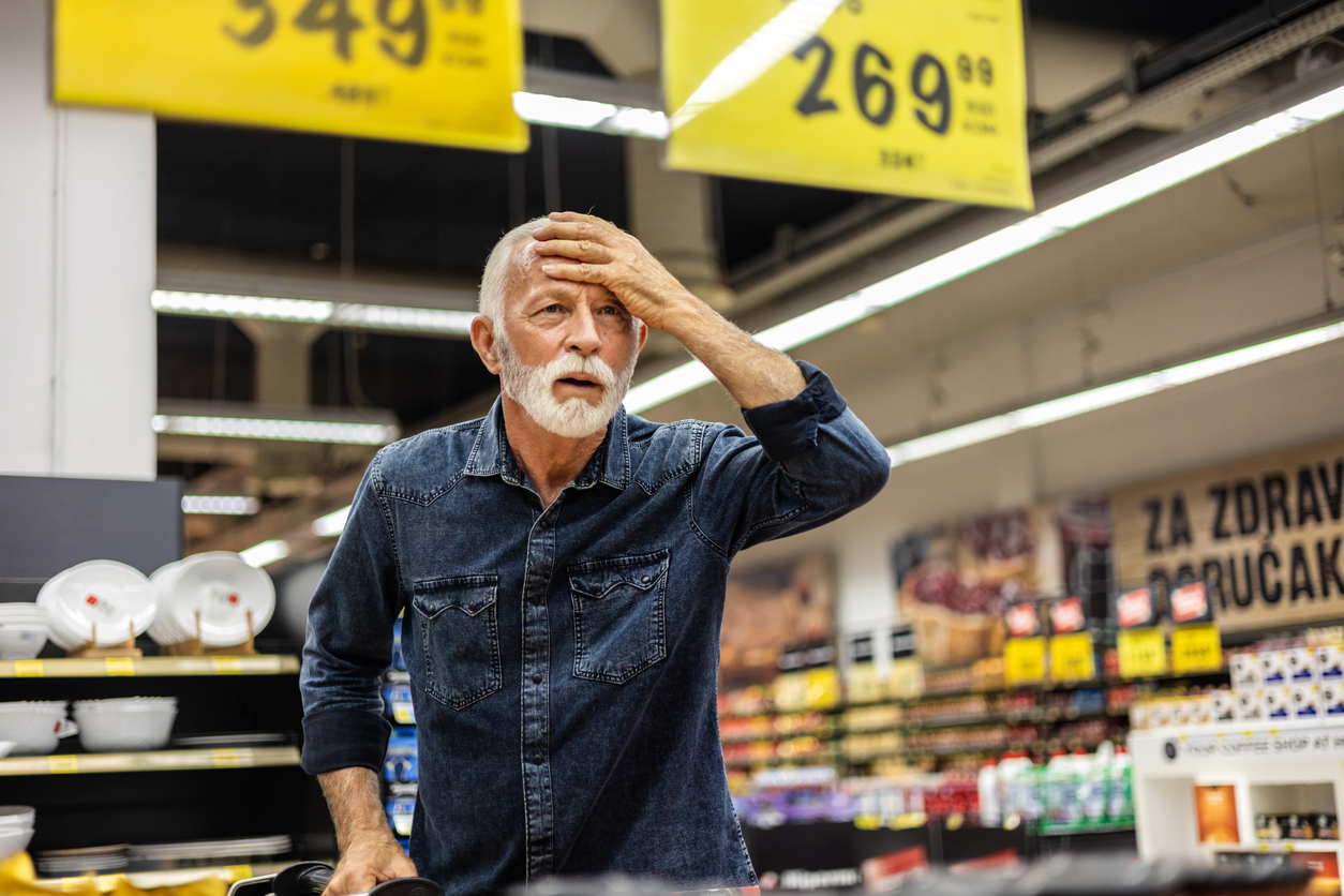 Grocery store, older bearded man, mid-frame close-up, daytime fluorescent light, editorial travel photo, one person.