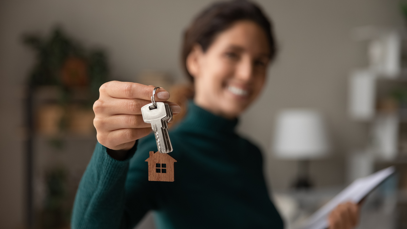 Home interior, house keys with wooden house-shaped keychain, woman foreground, daytime soft light, editorial travel photo, people.