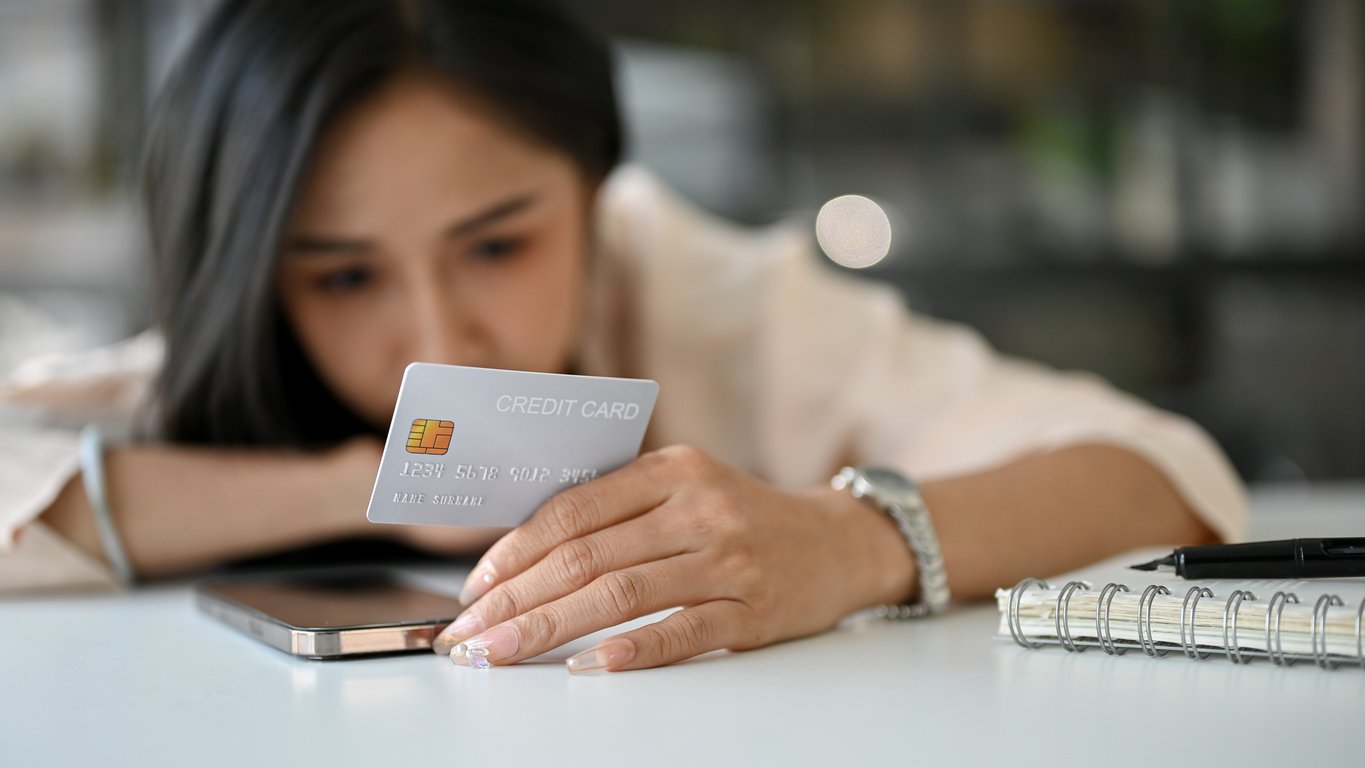 Tabletop scene, woman examining credit card, close-up with work items, daylight illumination, documentary style, one person.