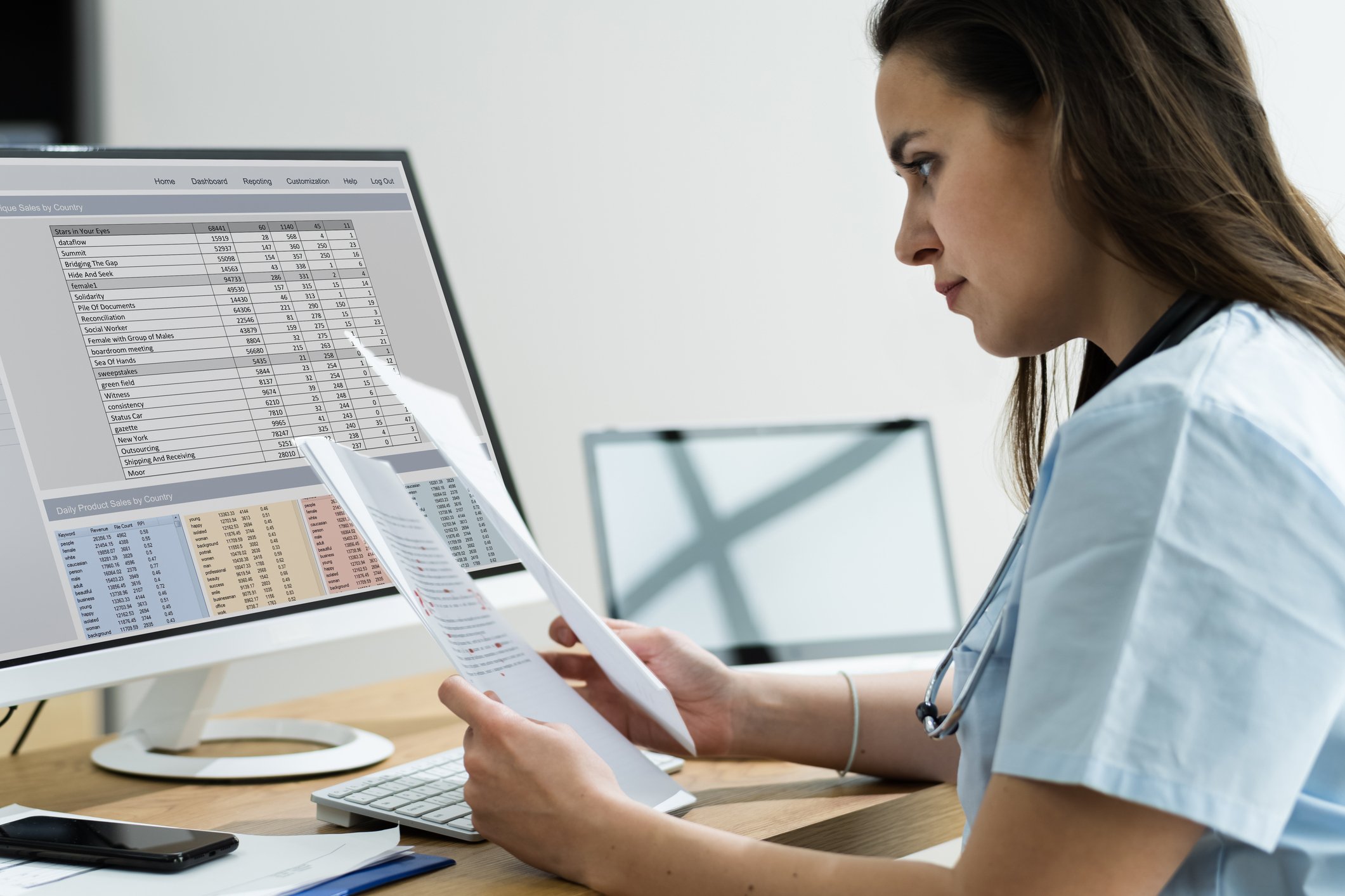 Medical office, charts and computer with spreadsheets, desk-level view, daytime window light, documentary style, one woman.