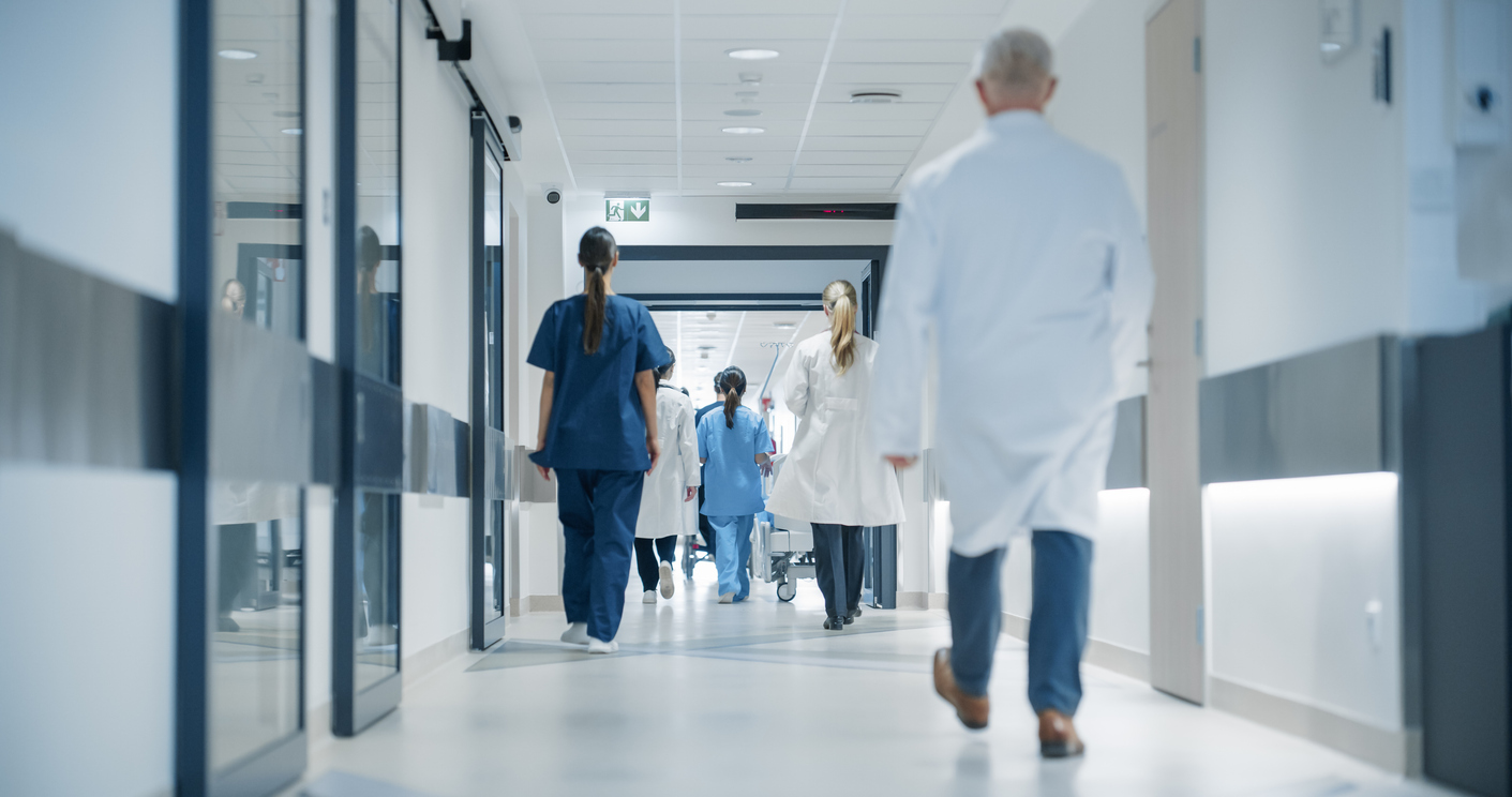 Hospital corridor, glass walls, reflective floors, bright daylight, documentary style, doctors and nurses present.