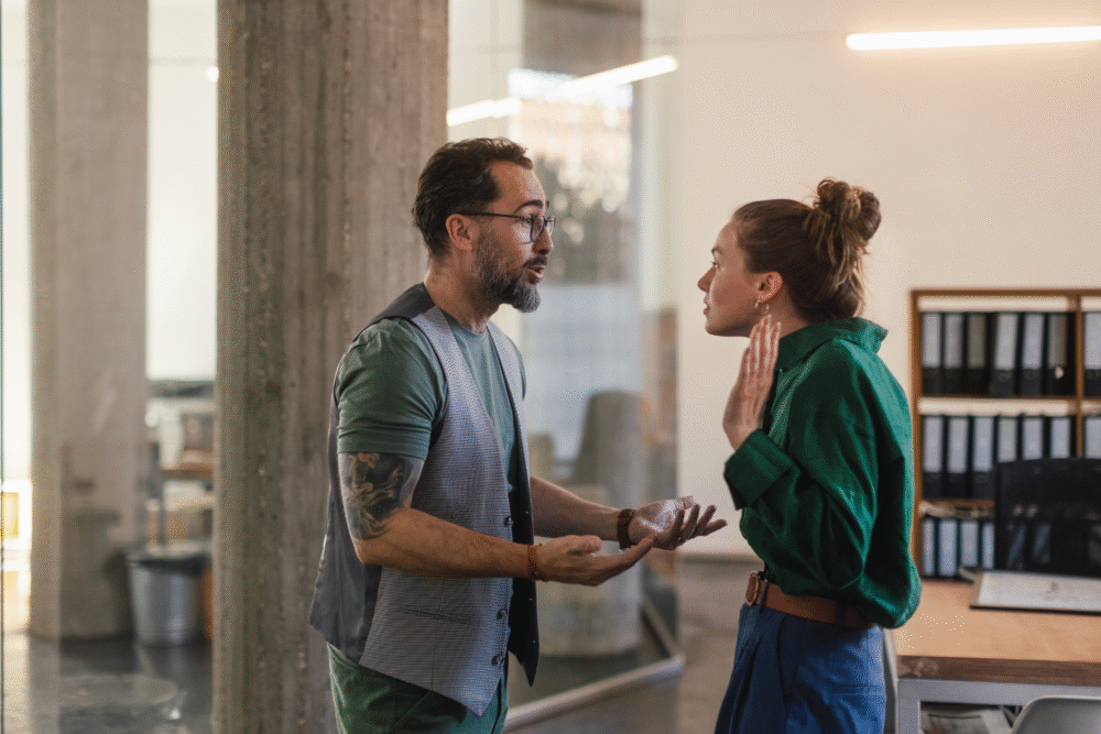 Office interior, two colleagues mid-argument, side view composition, daylight, documentary style, people present.