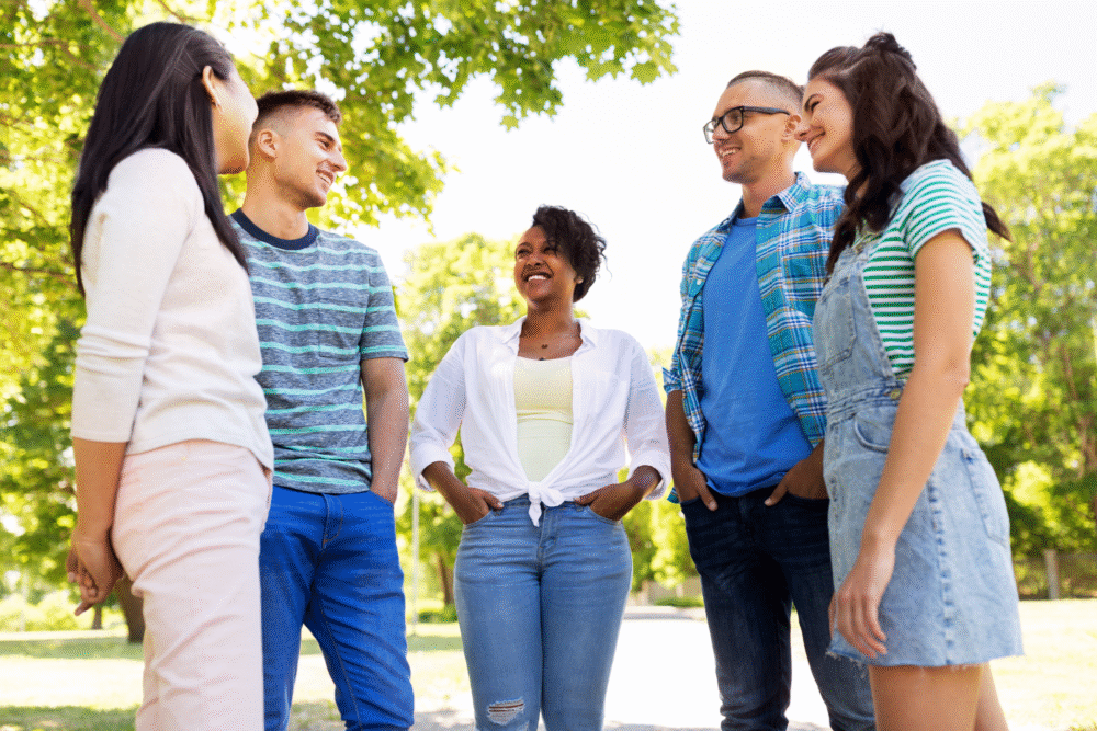 Park setting, group socializing, circular arrangement, daytime sunlight, editorial travel photo, five young adults.