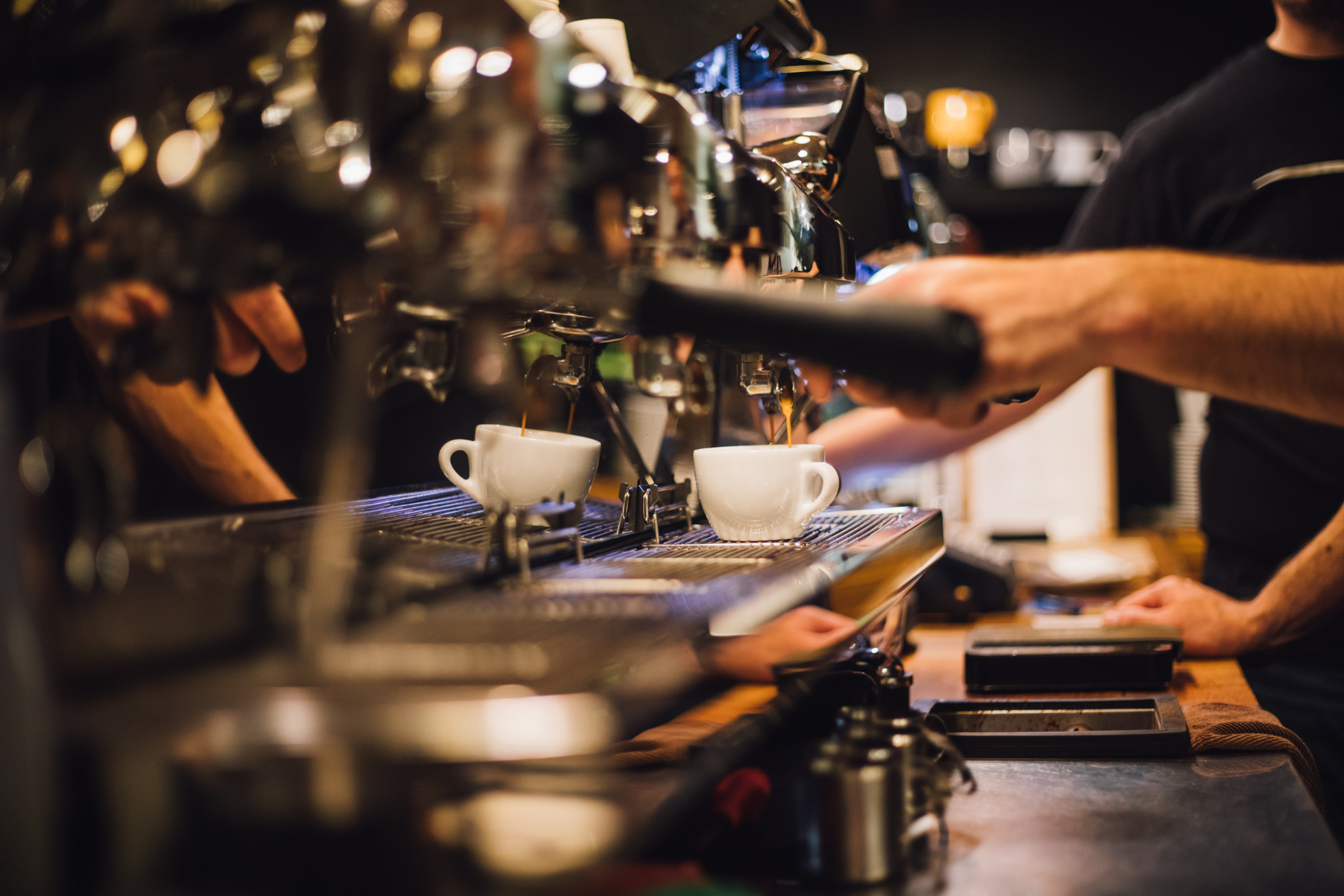 Cafe interior, barista hands with espresso machine, tight crop, warm dim lighting, editorial travel photo, no people visible.