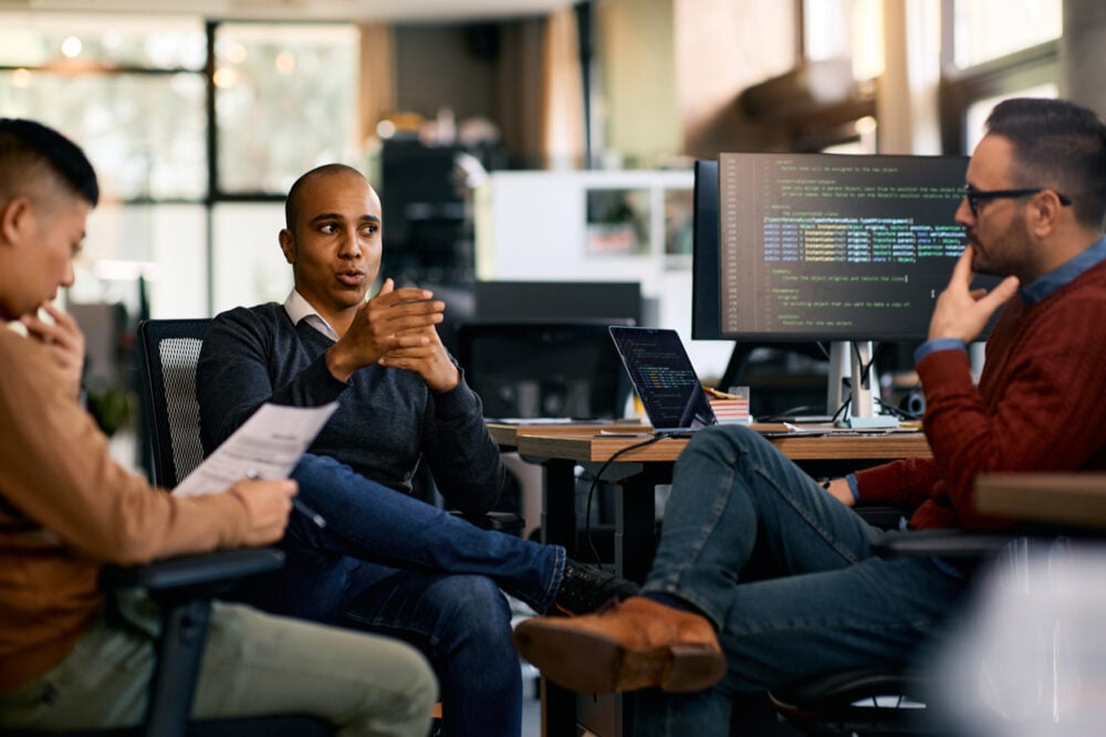 Office interior, group meeting, three men in discussion, midday lighting, documentary style, people.