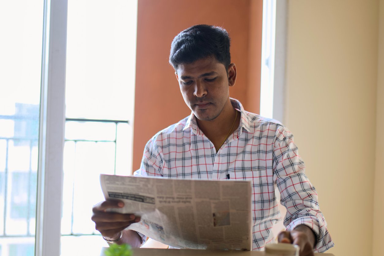 Indoor cafe, man reading newspaper at table, sunlight through window, soft morning light, editorial travel photo, one person.