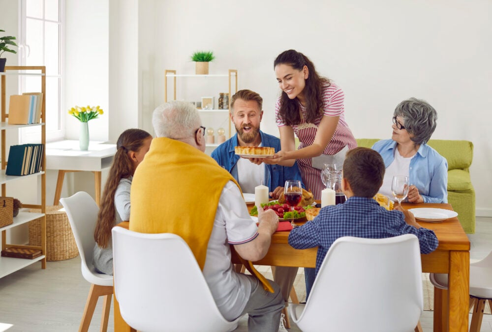 Cozy dining room, pie-serving young woman, family gathered at table, daytime natural light, editorial travel photo, six people.