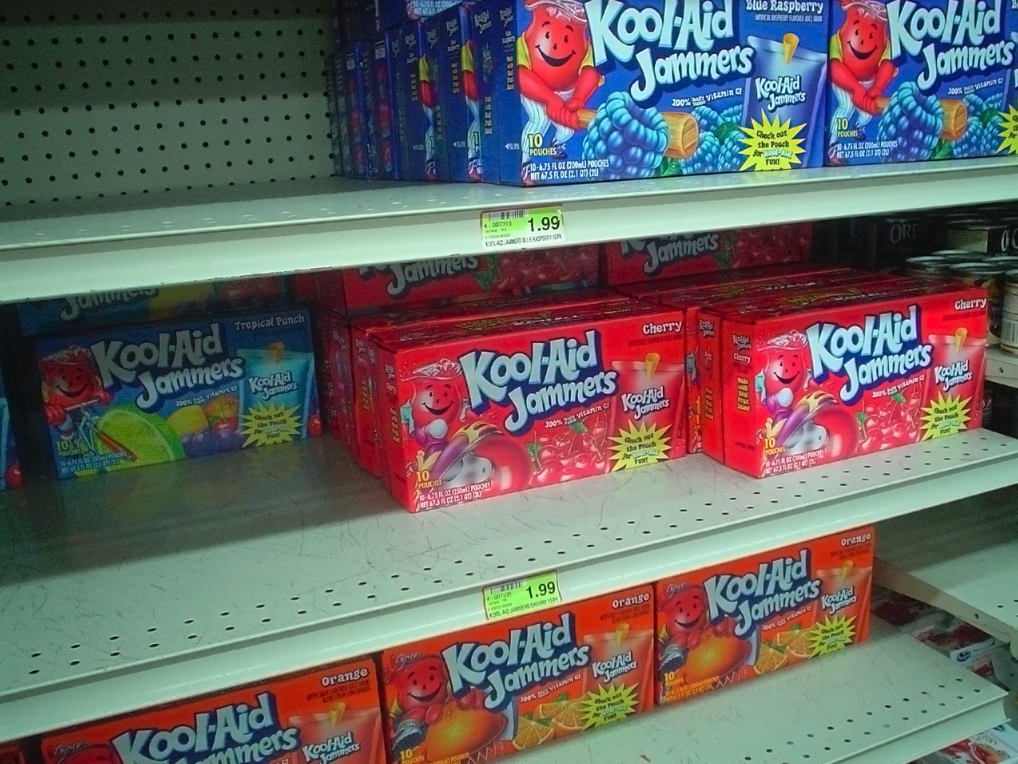 Grocery store shelves, Kool-Aid Jammers boxes, rows with gaps, bright retail lighting, editorial travel photo, no people.
