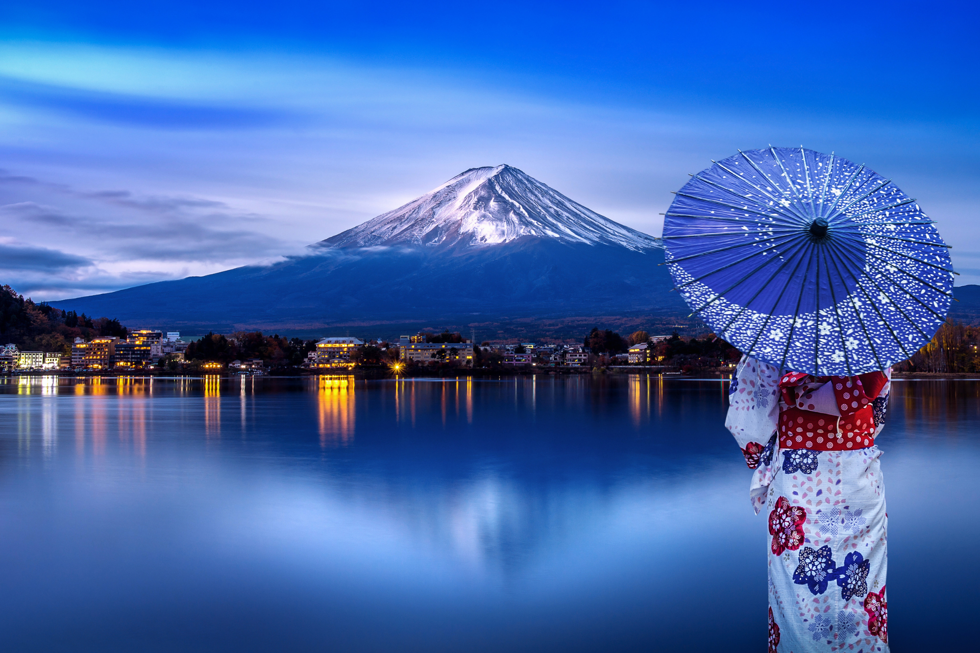 Lake shore, person in floral kimono with blue umbrella, Mount Fuji backdrop, evening glow, editorial travel photo, people.