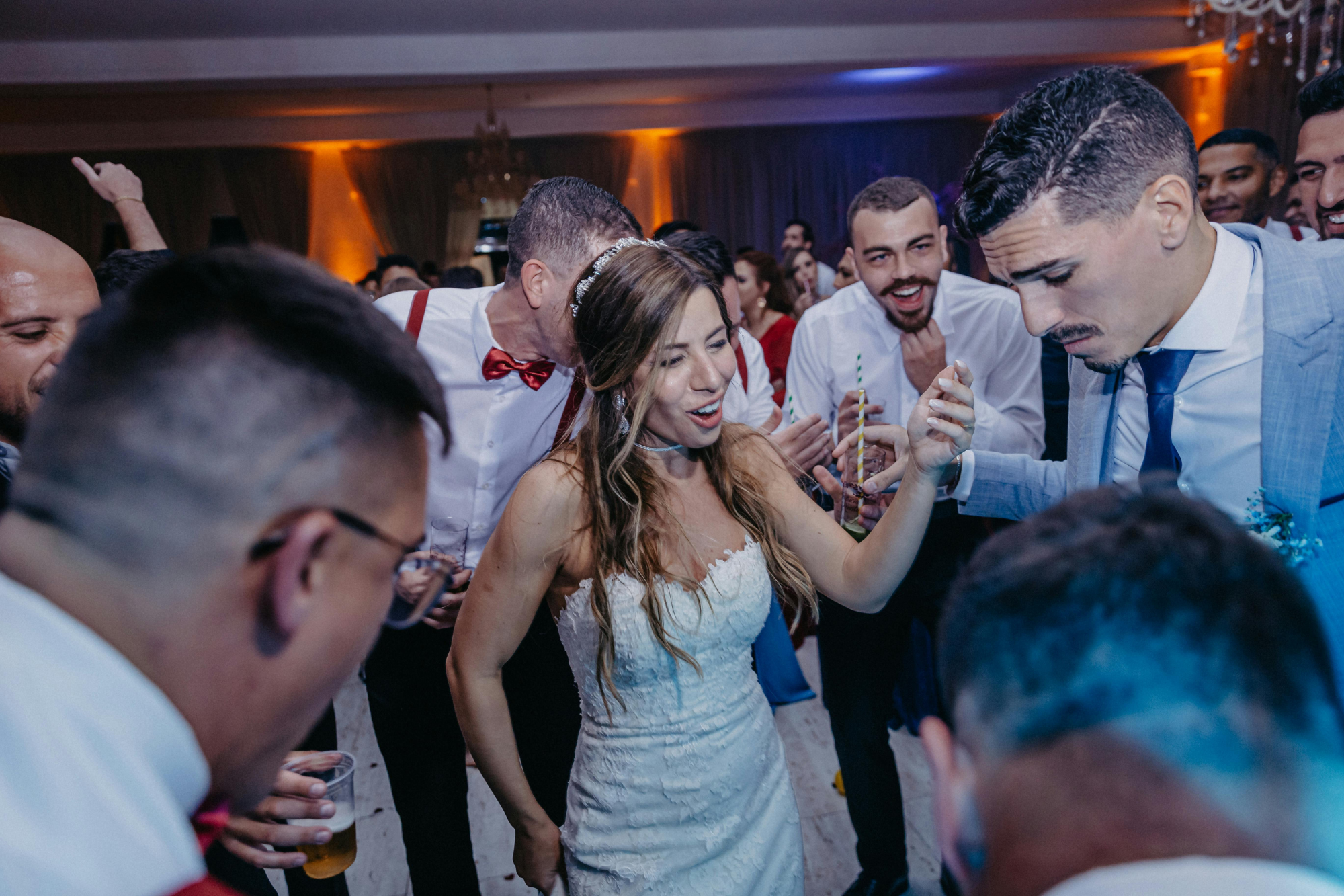 Wedding reception hall, joyful bride dancing center, surrounded by guests, evening light, documentary style, people celebrating.