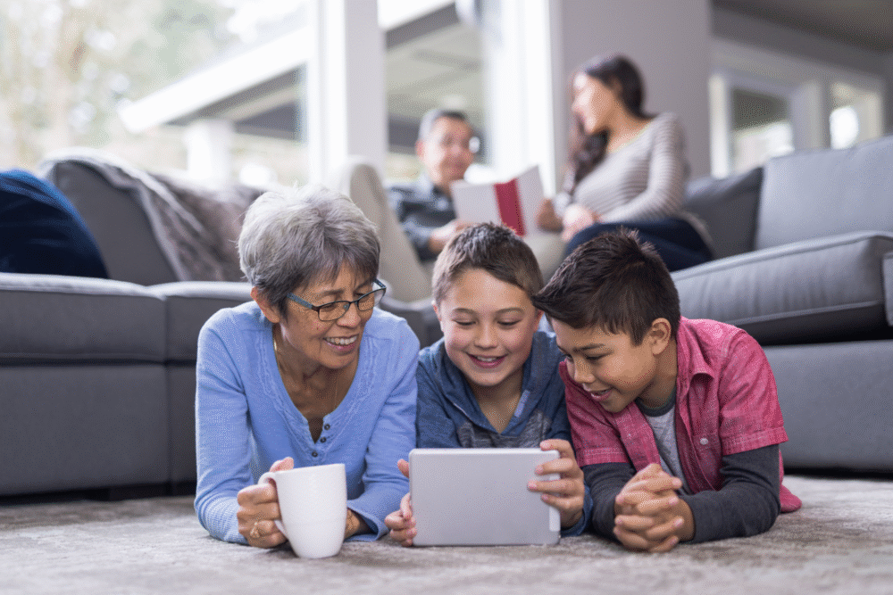 Bright living room, family gathered, foreground group on carpet, daylight streaming in, documentary style, people interacting.