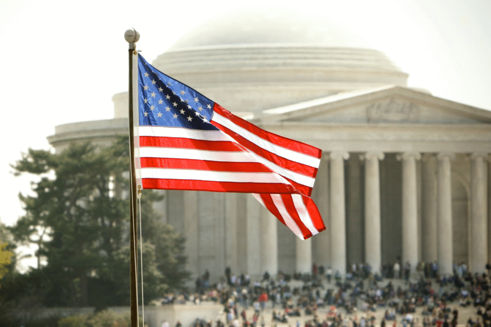 Jefferson Memorial, American flag foreground, crowd background, bright daylight, editorial travel photo, people visible.