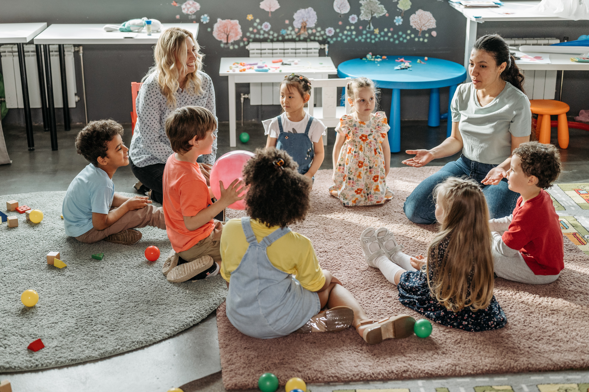 Classroom, children and adults in circle, toys scattered, daytime natural light, documentary style, people.