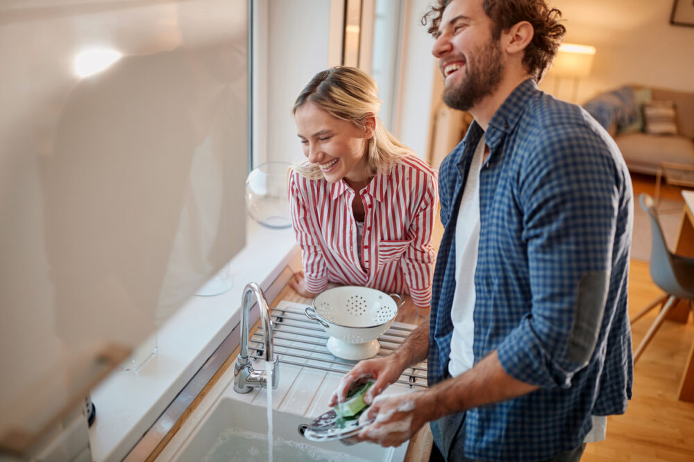 Kitchen interior, couple washing dishes, sunlight through window, warm afternoon glow, editorial travel photo, two people.