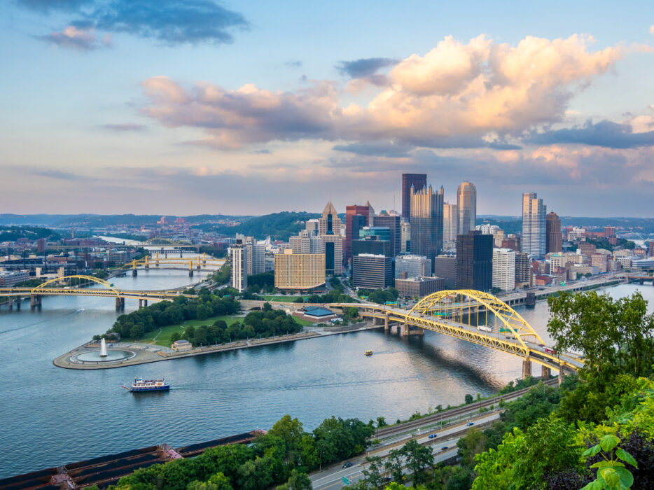 Downtown Pittsburgh, skyscrapers and yellow bridges, wide river view at sunset, editorial travel photo, no people.