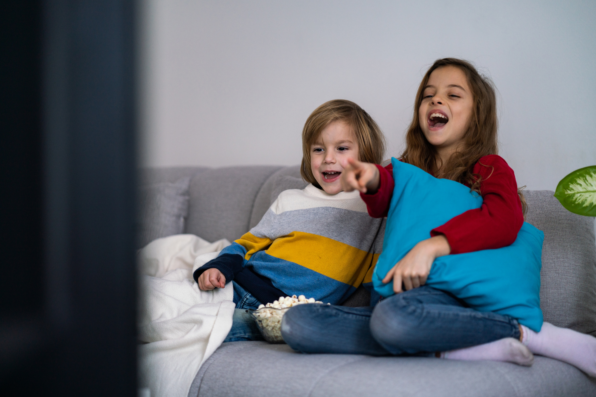 Living room, children with popcorn, two kids on couch mid-laughter, soft evening light, candid documentary style, people.