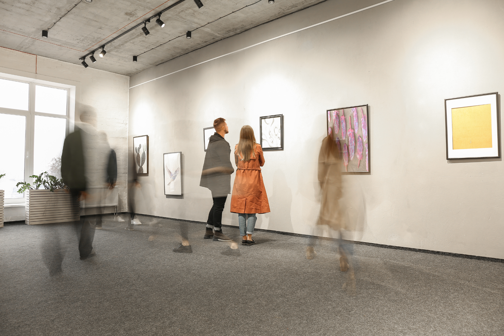 Modern art gallery interior, blurred figures in motion, framed artwork on walls, bright lighting, editorial travel photo, people.