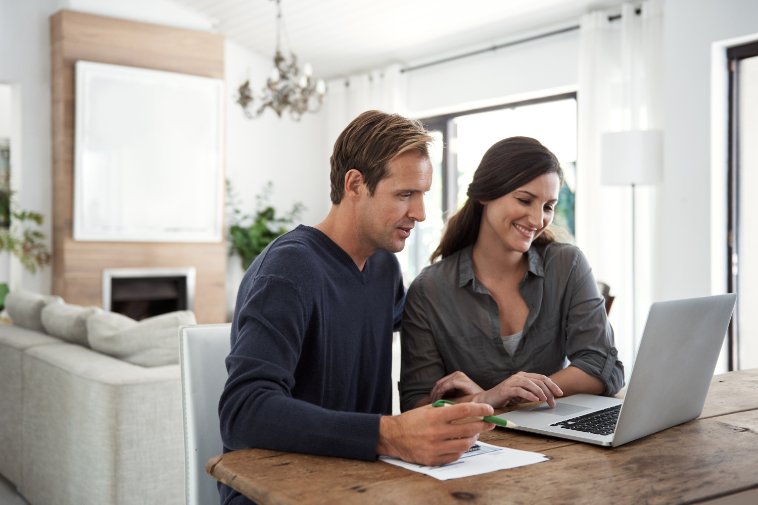 Bright living room, couple at laptop, wooden table foreground, midday natural light, documentary style, two people.