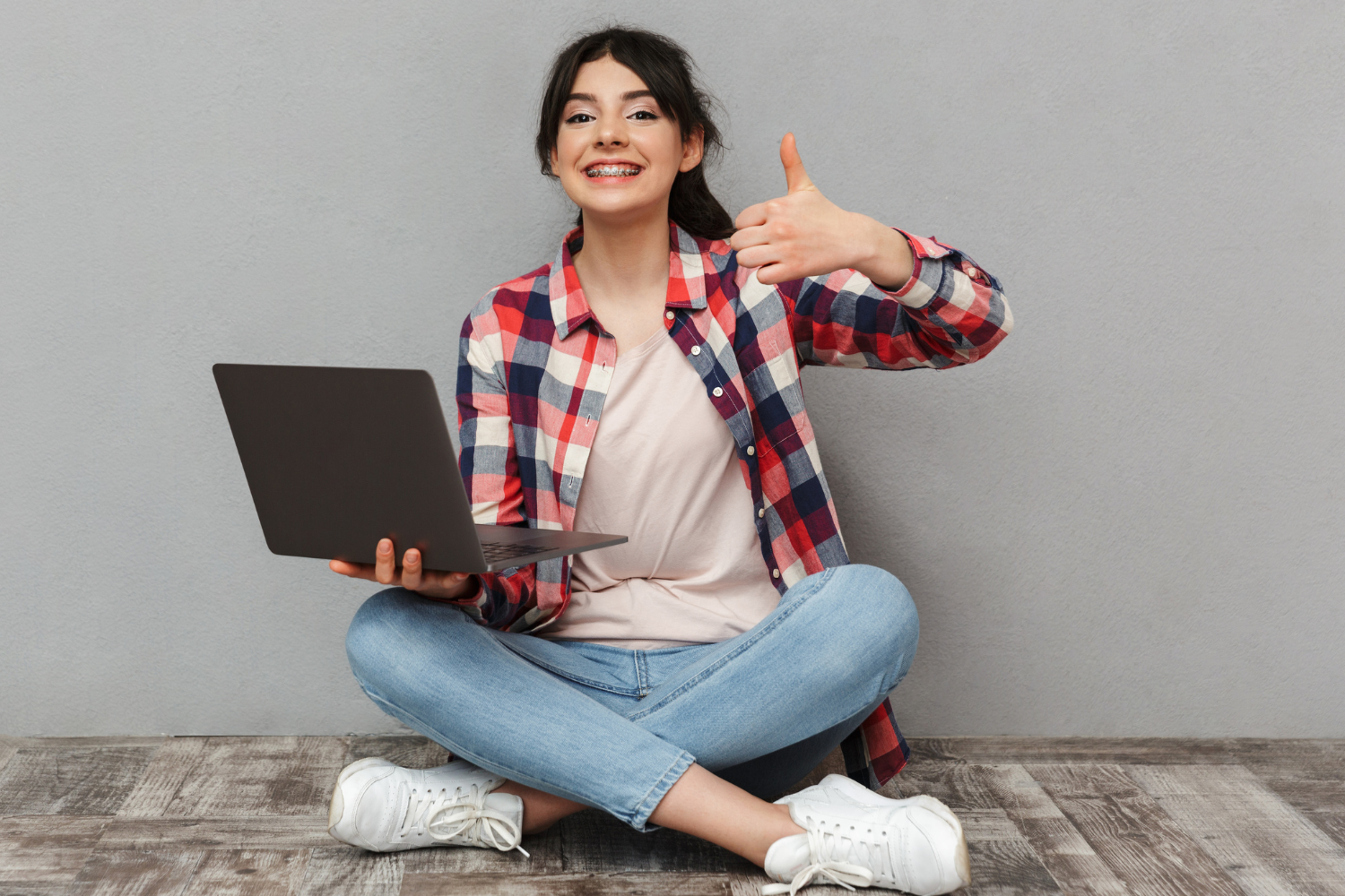 Indoor, woman with laptop and thumbs-up, cross-legged pose, bright even lighting, lifestyle editorial, one person.