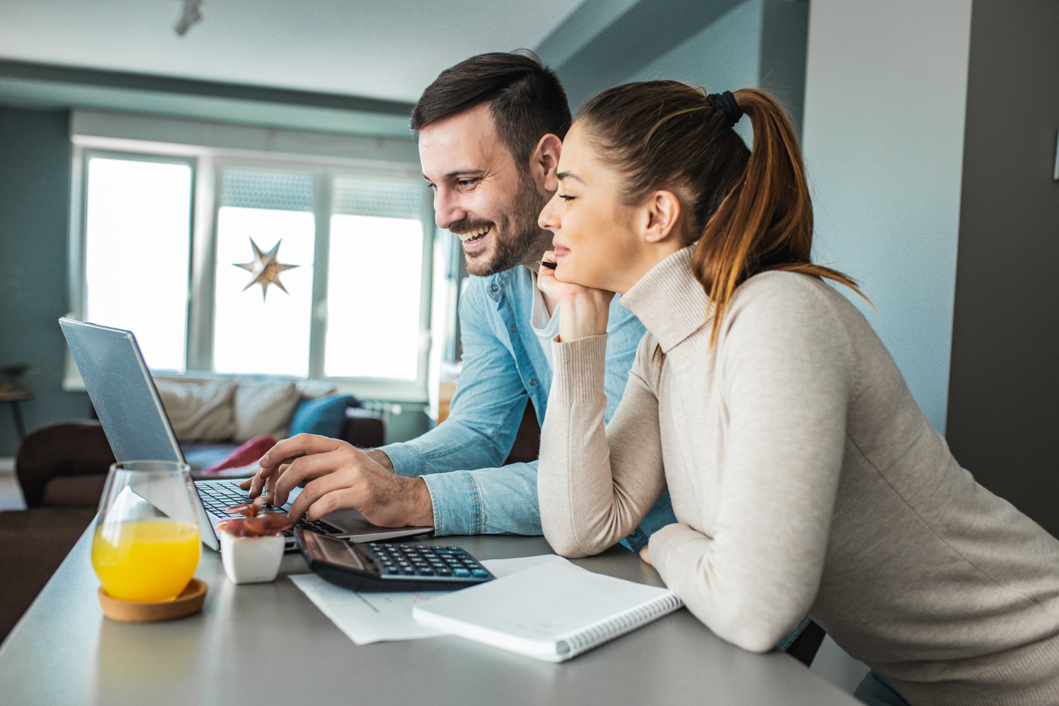 Kitchen counter, couple using laptop, notebook and glass on surface, daylight through windows, documentary style, two people.