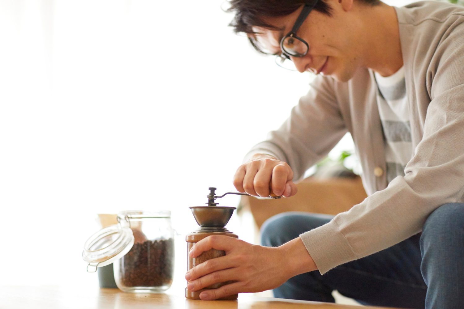 Cafe table, manual coffee grinder, close-up, soft daylight, editorial travel photo, single person present.