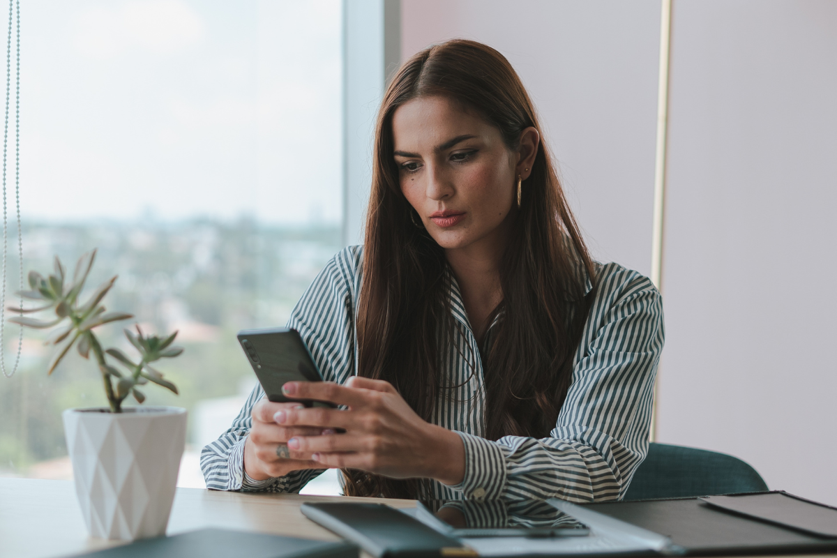 Window-side desk, woman with brown hair, smartphone focus, morning light, documentary style, one person.