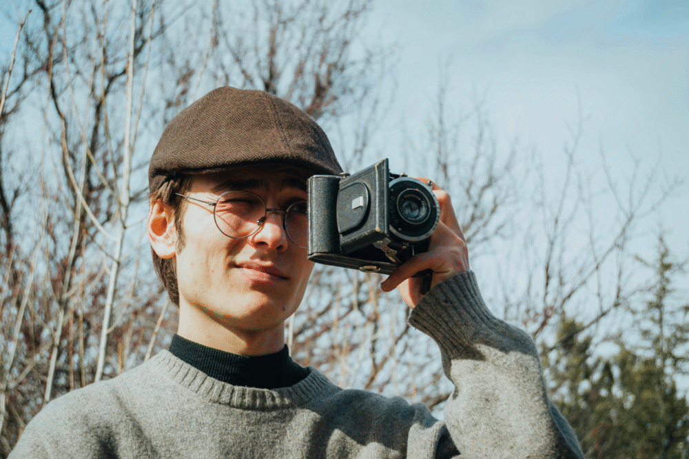 Outdoor setting, vintage camera close-up, centered composition, daytime natural light, editorial travel photo, one person present.