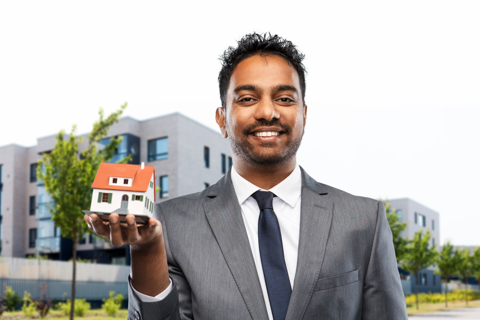 Modern apartment buildings, man in suit with model house, foreground focus, daylight, editorial travel photo, people visible.