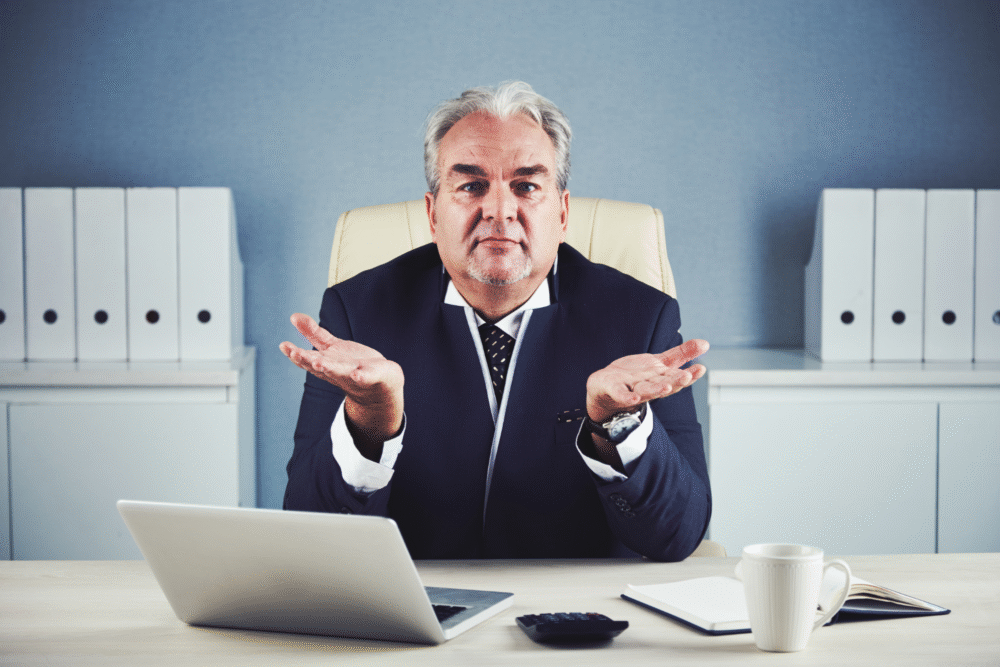 Office setting, man in suit at laptop, cluttered desk scene, daytime indoor light, documentary style, one adult present.