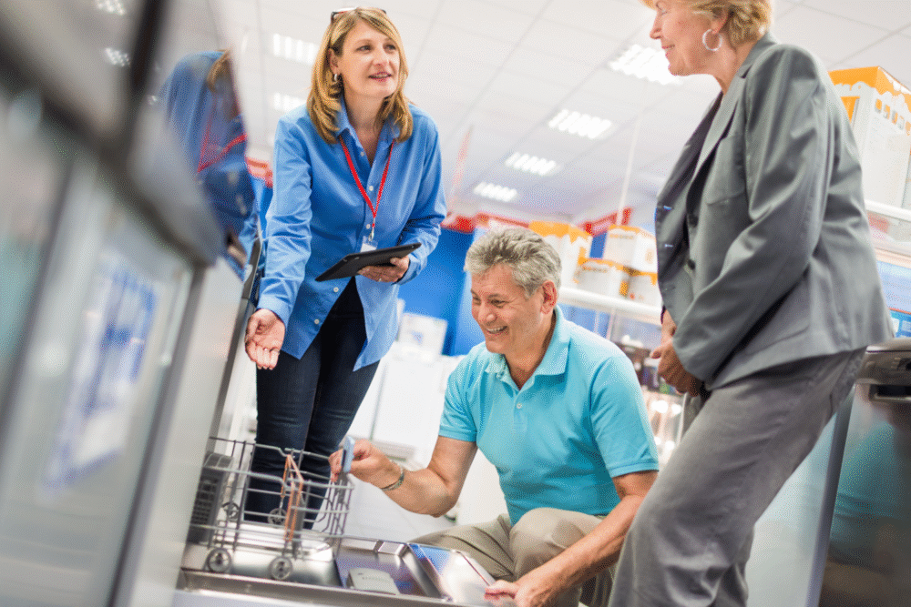 Store interior, dishwasher display center, trio in focused discussion, bright showroom lighting, documentary style, three people.