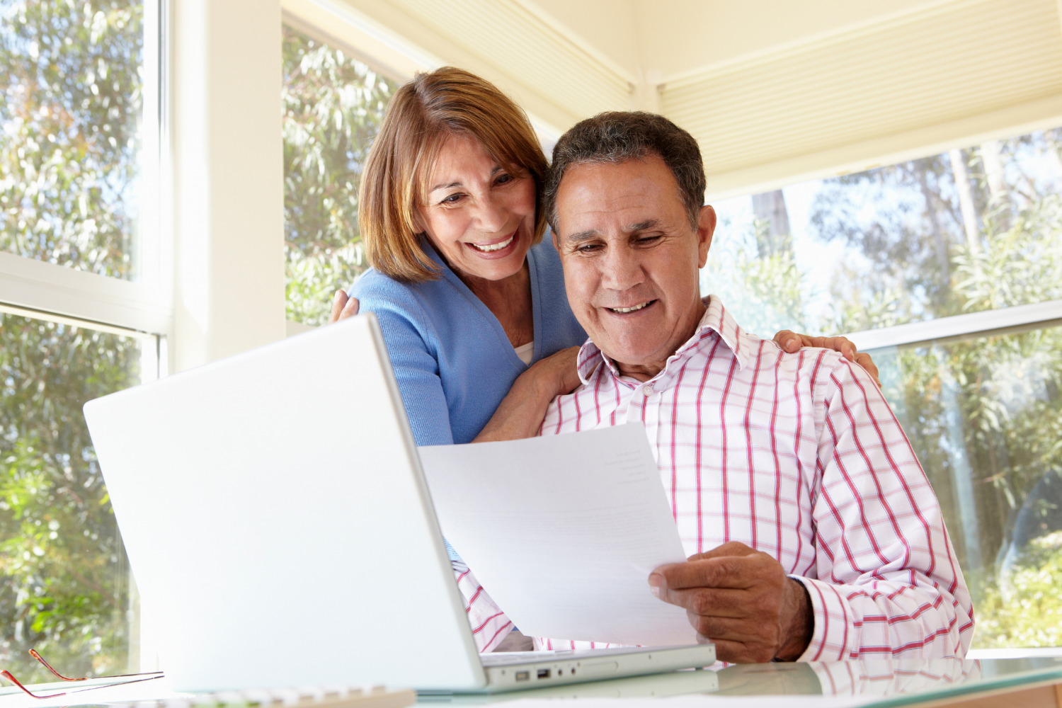 Sunny kitchen window, couple at table, paper and laptop foreground, morning light, documentary style, two smiling people.