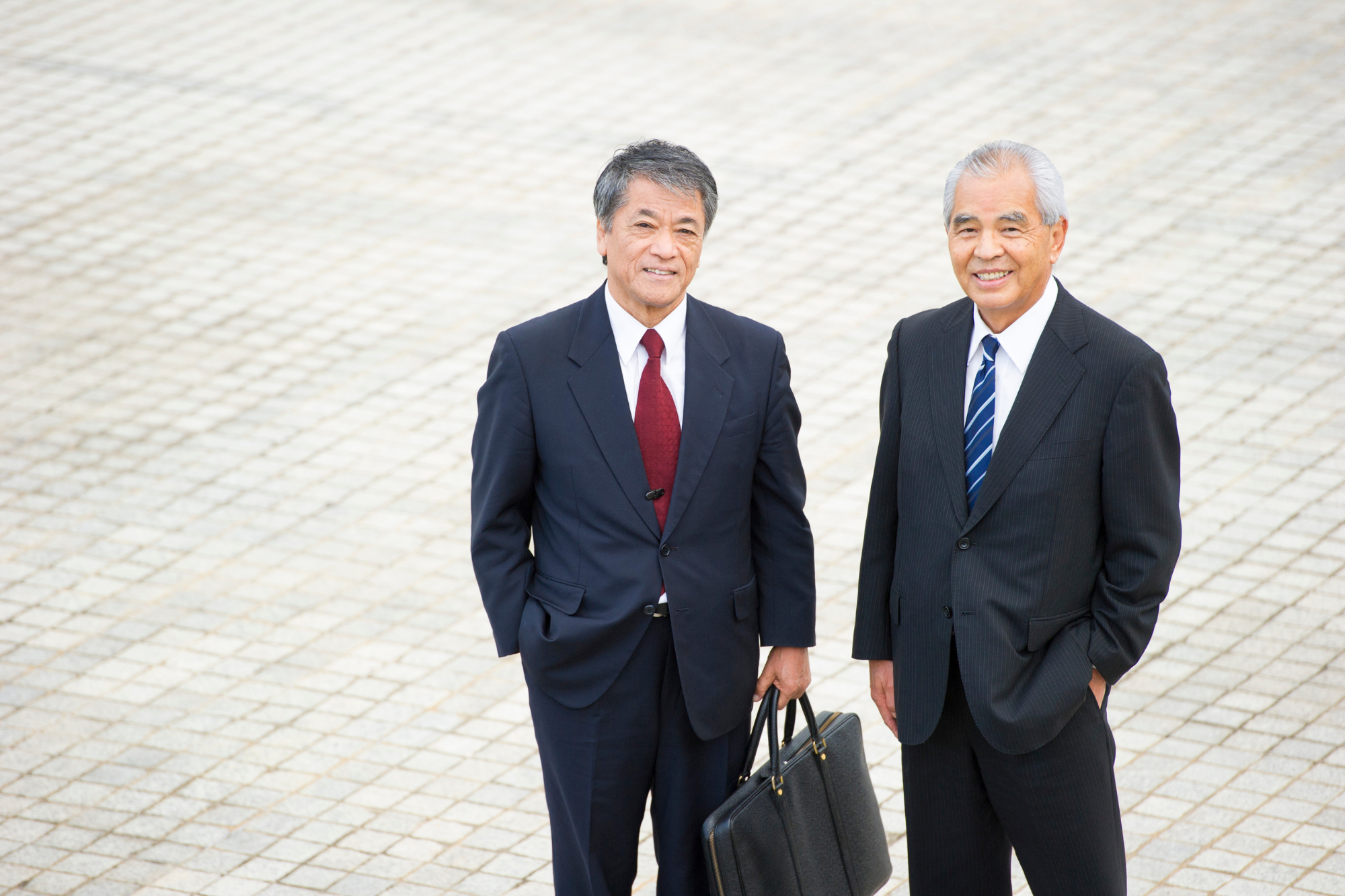 Tiled courtyard, two businessmen center frame, daytime sunlight, editorial travel photo, smiling, holding briefcase. People.