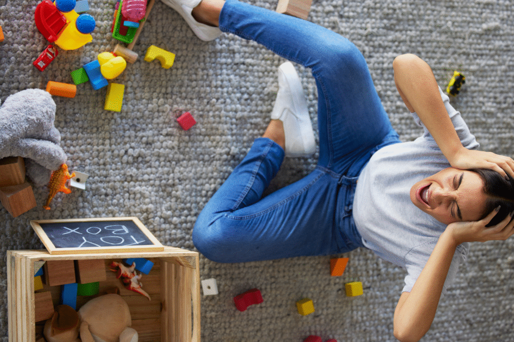 Carpeted living room, woman overwhelmed, toys strewn around open Toy Box, daytime natural light, documentary style, one person.
