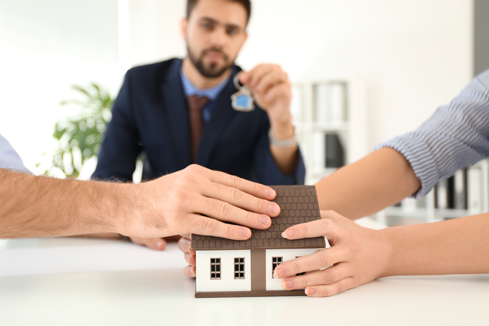 Office setting, model house and keys, group at table, daytime indoor light, documentary style, three people present.