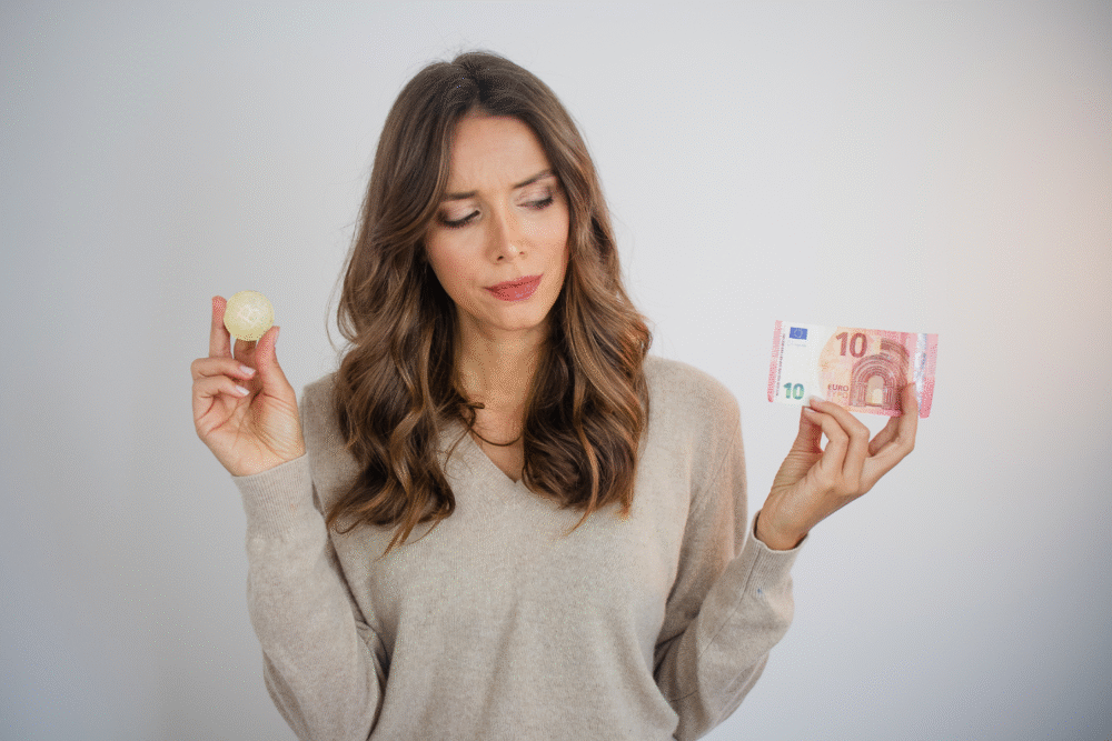 Plain background, woman comparing Bitcoin coin and 10 euro note, centered composition, soft light, editorial travel photo, one person.