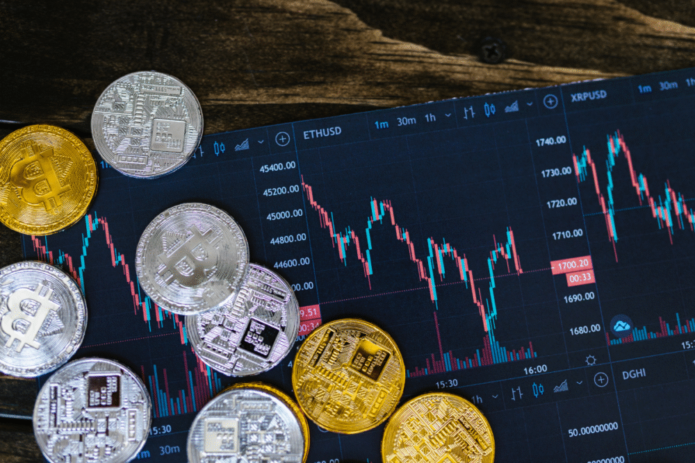 Dark tabletop, scattered gold and silver crypto coins, digital screen with charts behind, night lighting, editorial travel photo, no people.