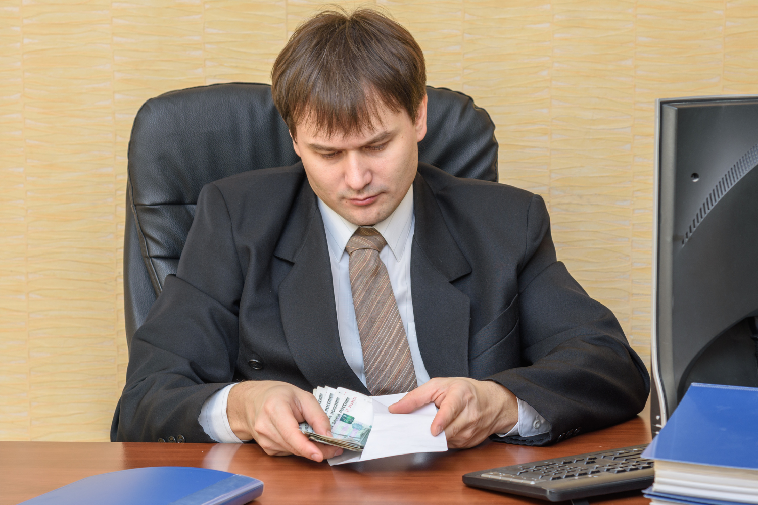 Office interior, suited man counting cash, sitting at cluttered desk, daytime ambient light, documentary style, one person.