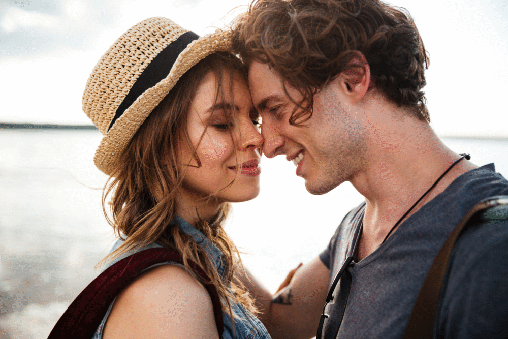 Beach, smiling couple with foreheads touching, waist-up composition, soft daylight, editorial travel photo, people.