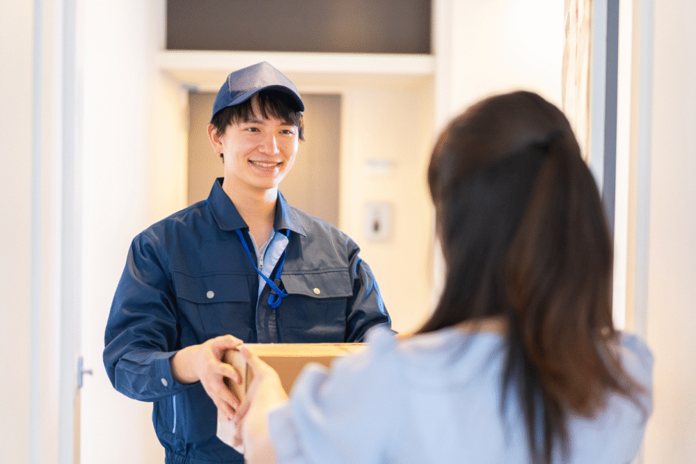 Bright hallway entryway, delivery exchange at doorway, frontal composition, daytime natural light, editorial travel photo, two people.