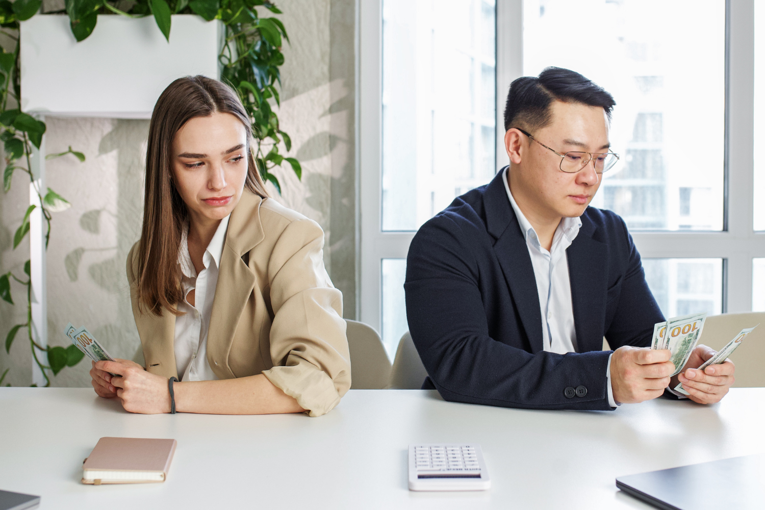 Office desk, woman glancing at man counting cash, side-by-side composition, daytime light, documentary style, with people.