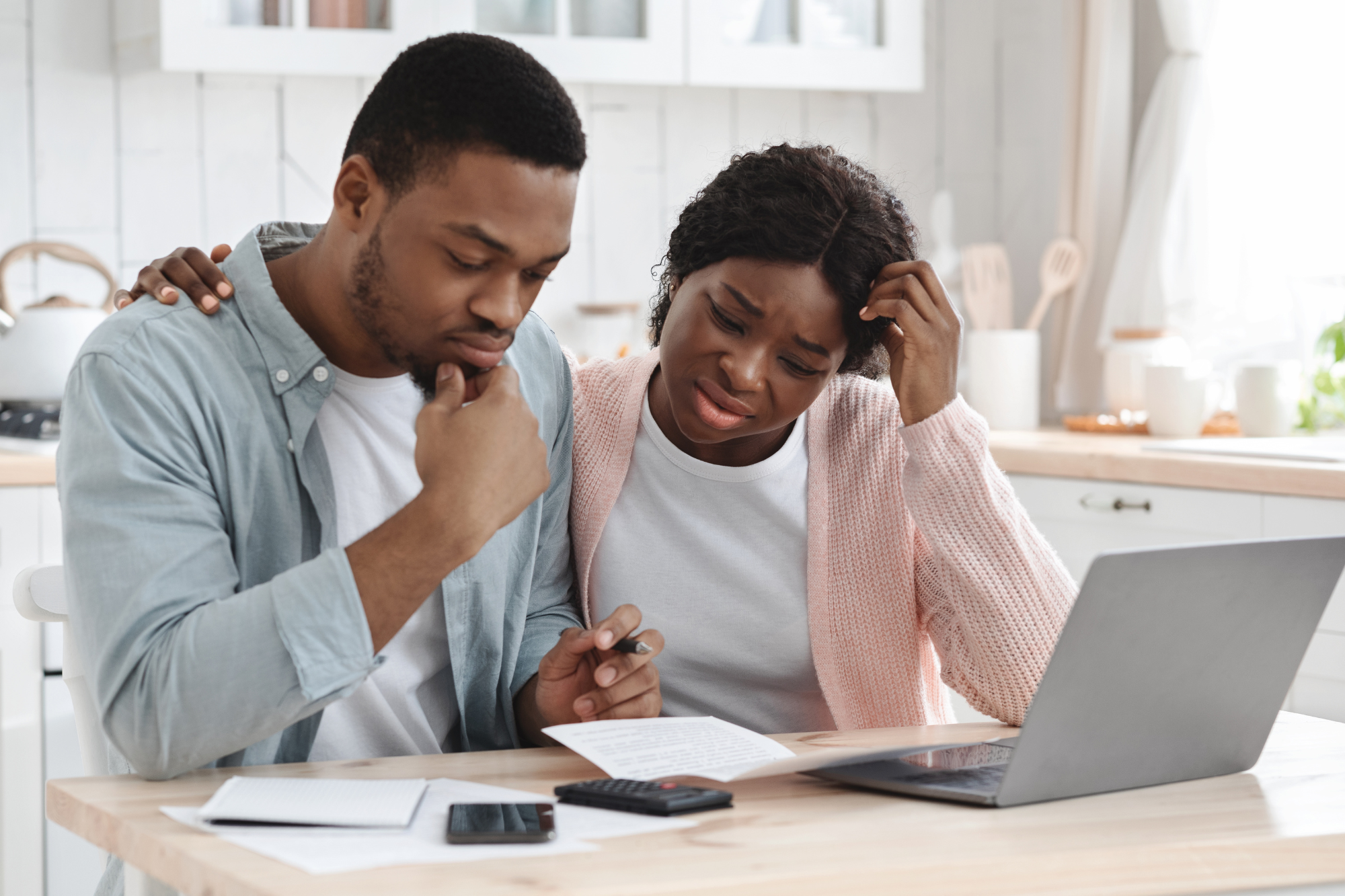 Bright kitchen, financial documents, laptop and calculator on table, morning light, documentary style, stressed couple present.